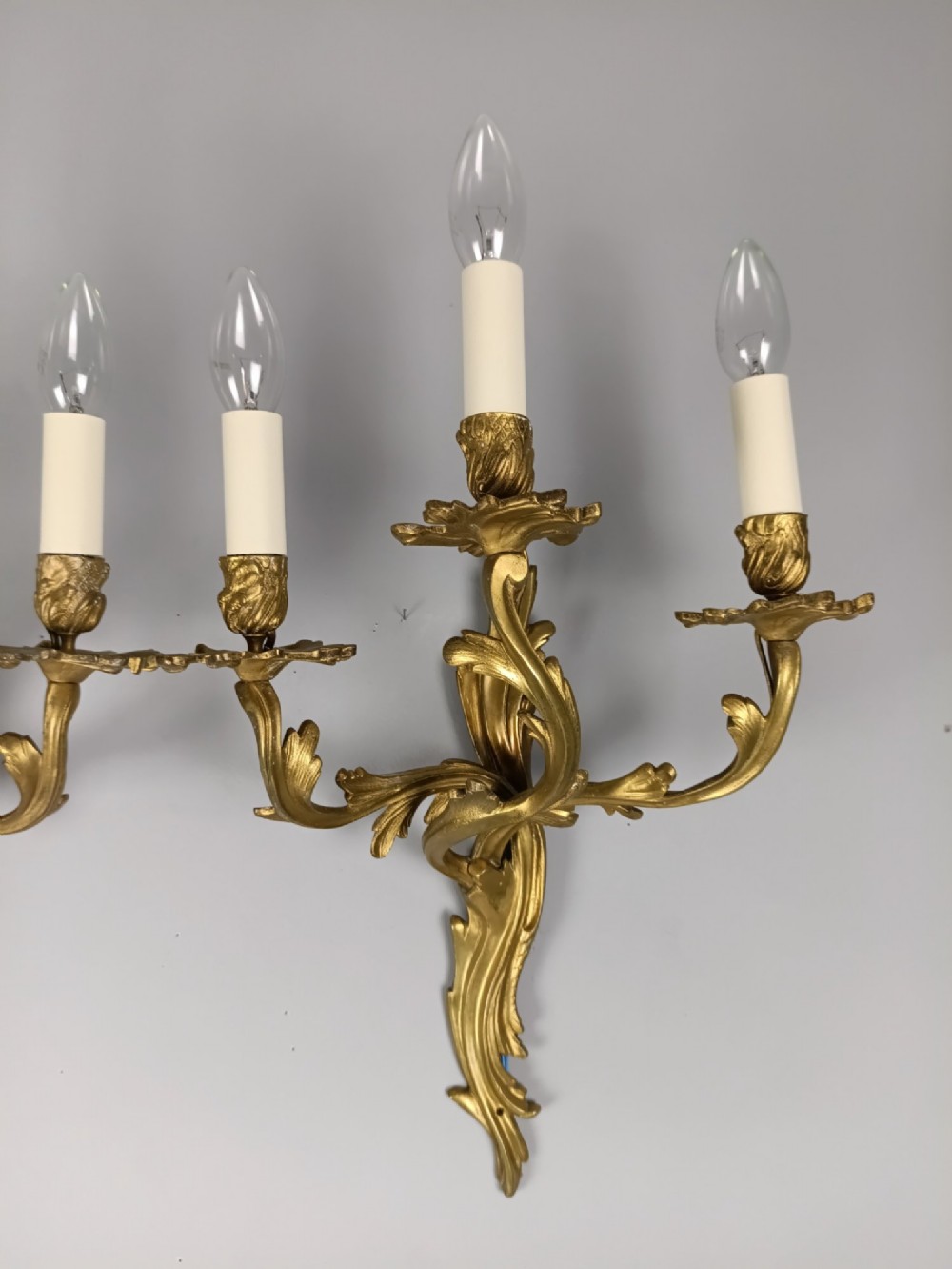 A pair of antique French Rococo gilded bronze triple-arm wall sconces featuring acanthus leaf scrollwork and candle sleeves. View V