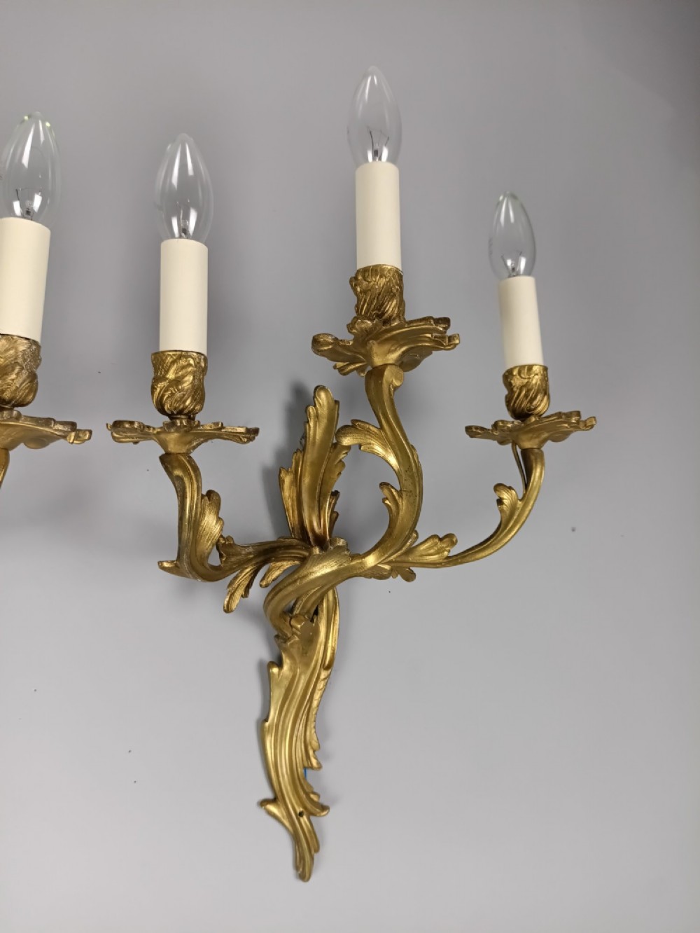 A pair of antique French Rococo gilded bronze triple-arm wall sconces featuring acanthus leaf scrollwork and candle sleeves. View VI