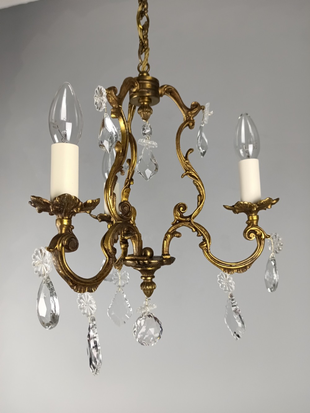 A French Rococo style three-light gilded brass chandelier decorated with suspended cut crystal drops and candle-effect light holders.