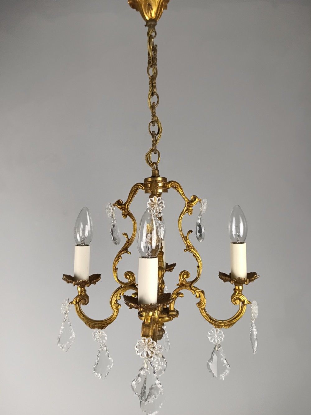A French Rococo style three-light gilded brass chandelier decorated with suspended cut crystal drops and candle-effect light holders. View III
