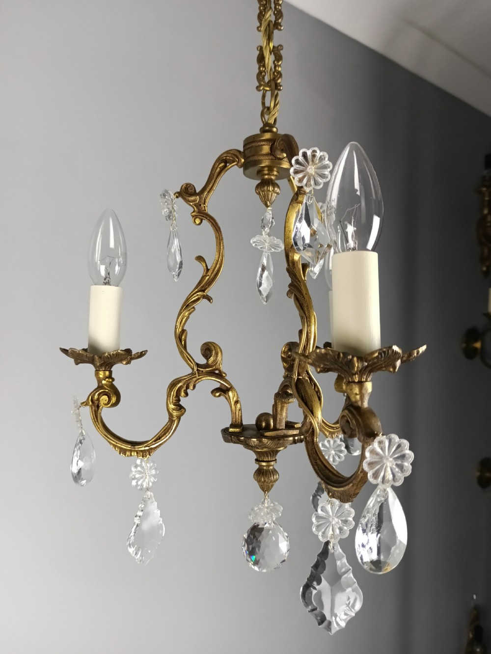A French Rococo style three-light gilded brass chandelier decorated with suspended cut crystal drops and candle-effect light holders. View IV