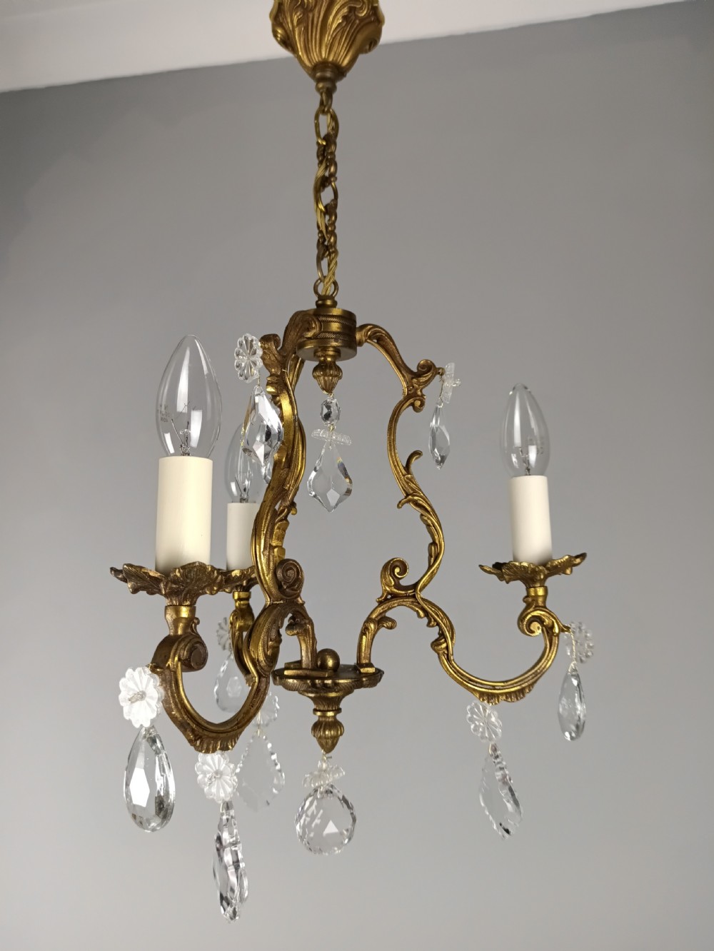 A French Rococo style three-light gilded brass chandelier decorated with suspended cut crystal drops and candle-effect light holders. View V