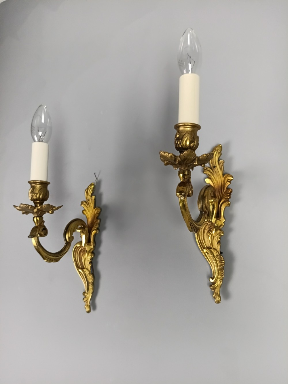 A pair of French gilt brass single-arm wall lights with acanthus leaf backplates and candle bulb fittings.