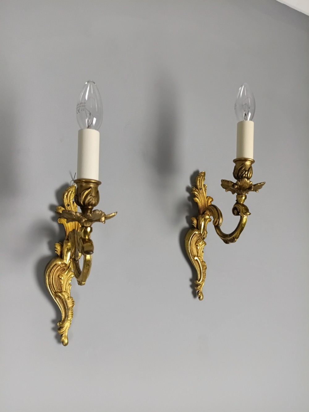 A pair of French gilt brass single-arm wall lights with acanthus leaf backplates and candle bulb fittings. View V