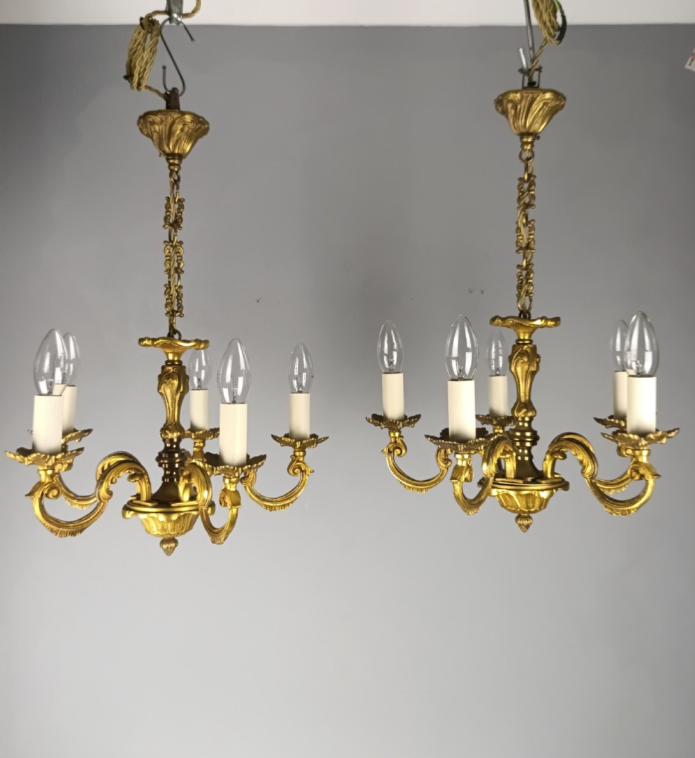 A matching pair of five-arm French gilt brass chandeliers featuring scrolling foliate arms, candle-effect sockets, and decorative hanging chains.