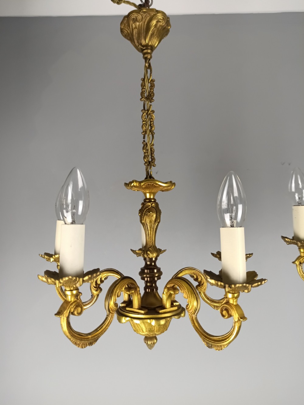 A matching pair of five-arm French gilt brass chandeliers featuring scrolling foliate arms, candle-effect sockets, and decorative hanging chains. View II