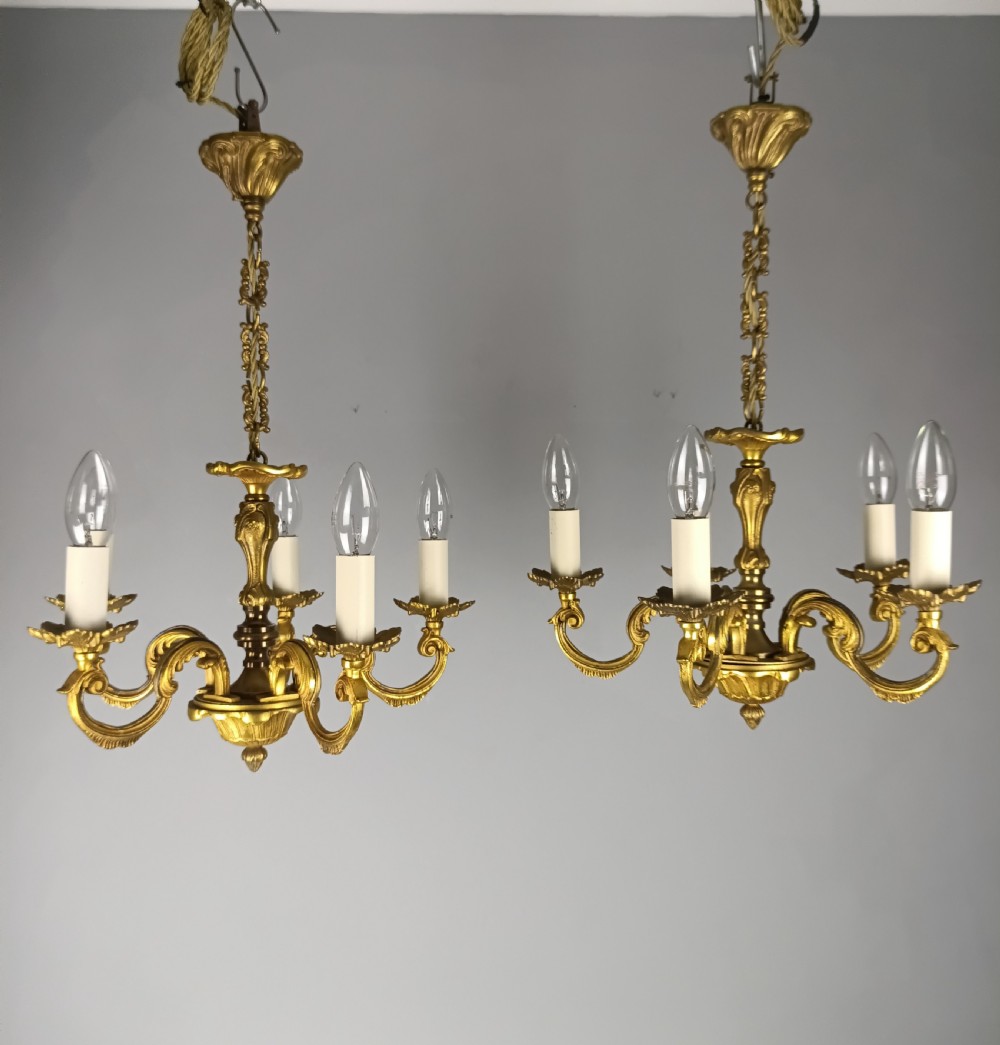 A matching pair of five-arm French gilt brass chandeliers featuring scrolling foliate arms, candle-effect sockets, and decorative hanging chains. View III