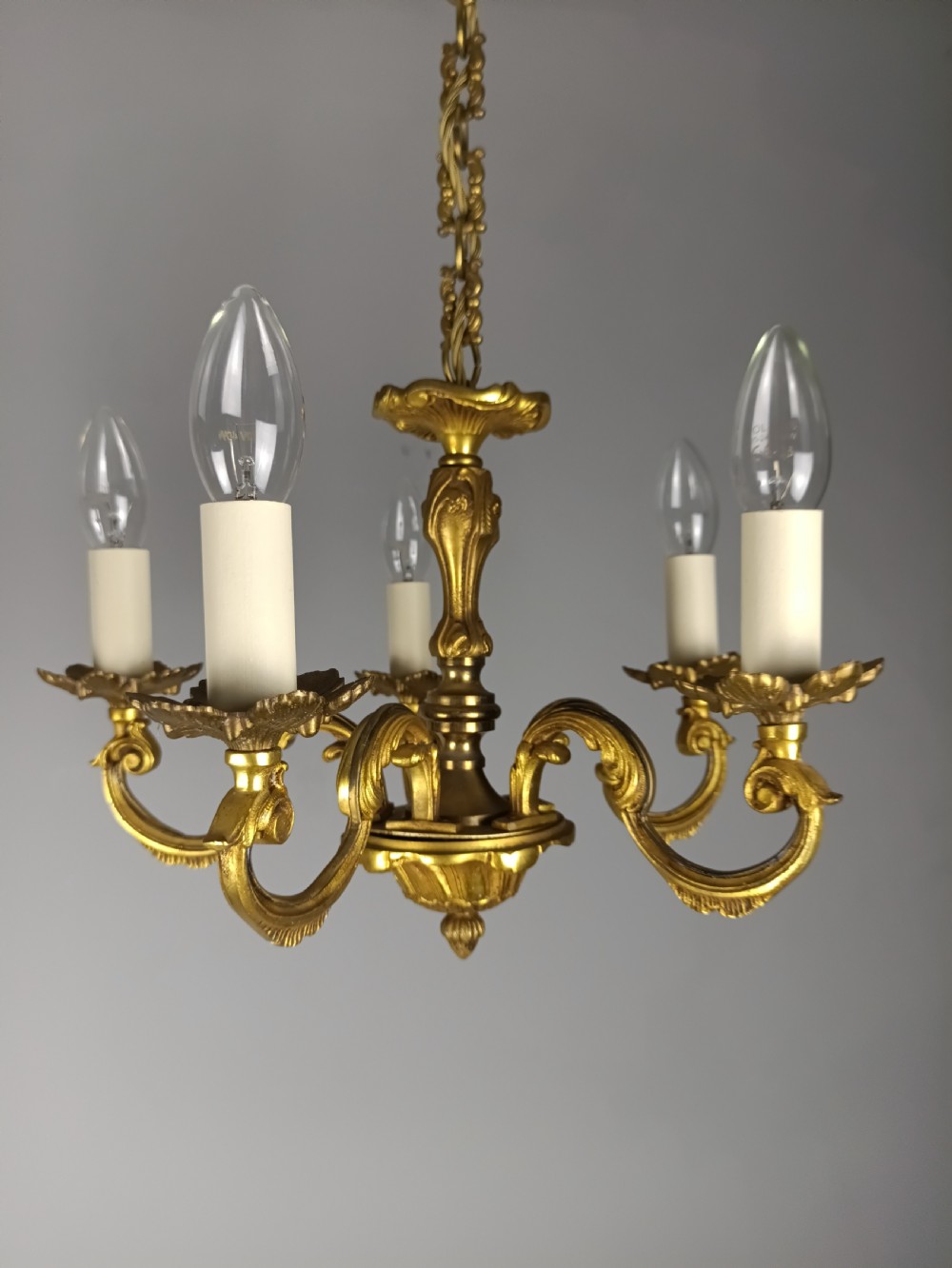 A matching pair of five-arm French gilt brass chandeliers featuring scrolling foliate arms, candle-effect sockets, and decorative hanging chains. View IV