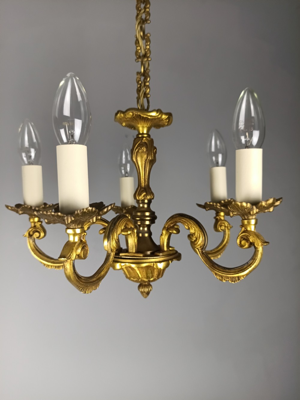 A matching pair of five-arm French gilt brass chandeliers featuring scrolling foliate arms, candle-effect sockets, and decorative hanging chains. View V
