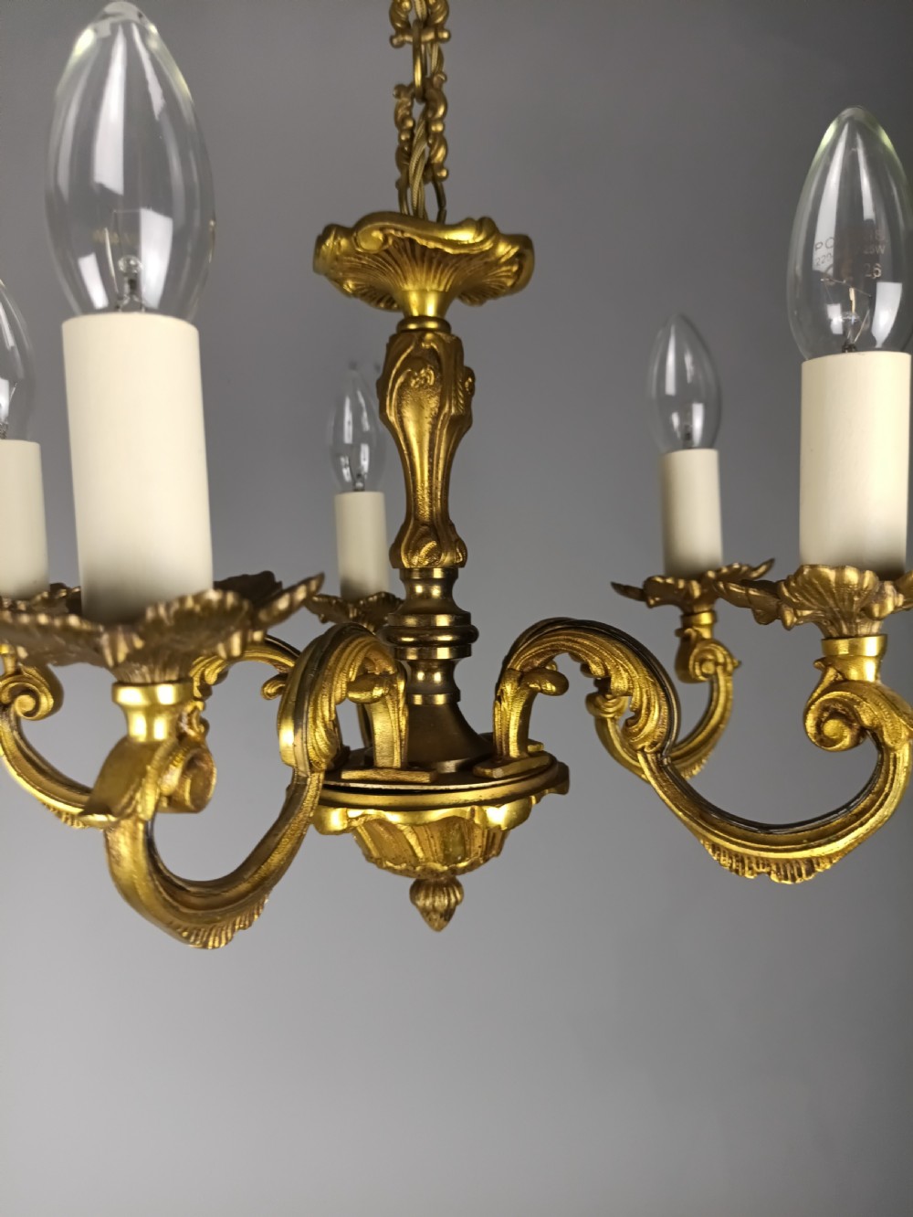 A matching pair of five-arm French gilt brass chandeliers featuring scrolling foliate arms, candle-effect sockets, and decorative hanging chains. View VI