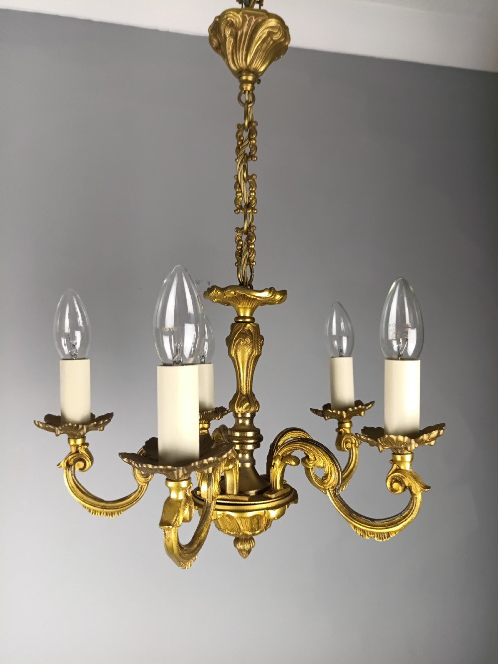 A matching pair of five-arm French gilt brass chandeliers featuring scrolling foliate arms, candle-effect sockets, and decorative hanging chains. View IX