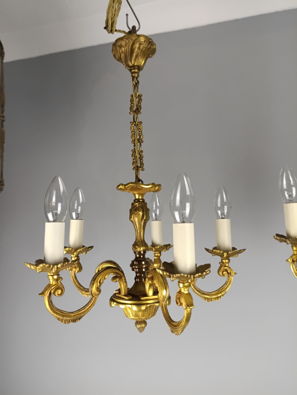 A matching pair of five-arm French gilt brass chandeliers featuring scrolling foliate arms, candle-effect sockets, and decorative hanging chains. View X
