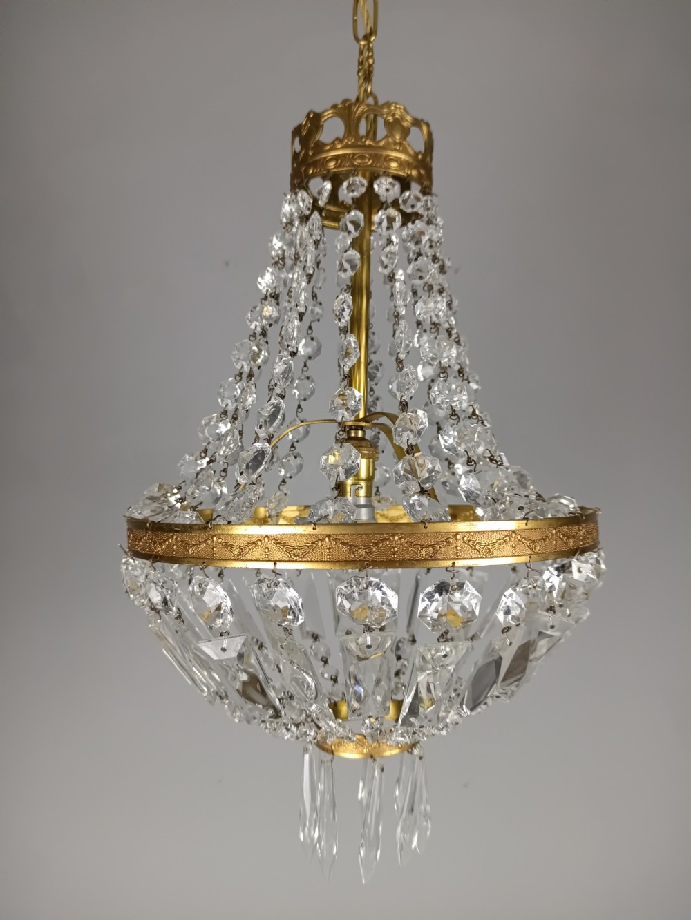 An antique French tent and bag chandelier featuring cascading crystal beads attached to a decorative brass rim with cut glass prisms below.