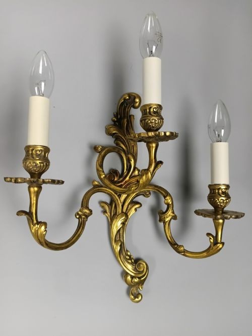 A pair of ornate gilded brass wall lights featuring three curving candle arms and Rococo scrollwork. View II