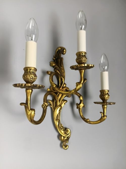 A pair of ornate gilded brass wall lights featuring three curving candle arms and Rococo scrollwork. View IV