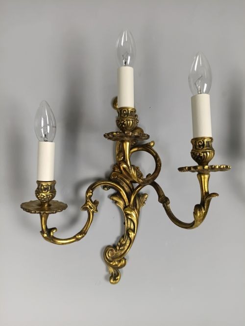 A pair of ornate gilded brass wall lights featuring three curving candle arms and Rococo scrollwork. View V