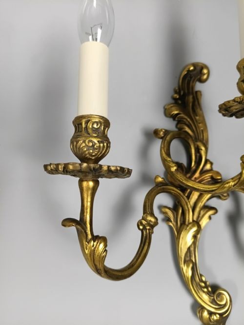 A pair of ornate gilded brass wall lights featuring three curving candle arms and Rococo scrollwork. View VII