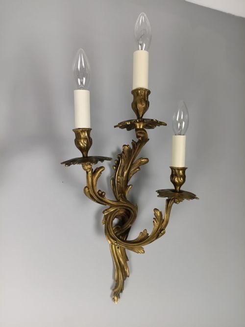 A pair of French Rococo style gilded bronze triple-arm wall sconces featuring ornate acanthus leaf scrollwork and candle-effect bulbs. View IV