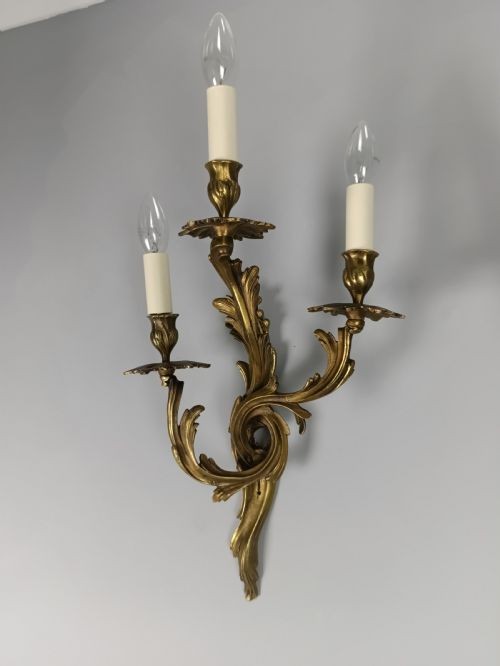 A pair of French Rococo style gilded bronze triple-arm wall sconces featuring ornate acanthus leaf scrollwork and candle-effect bulbs. View VI