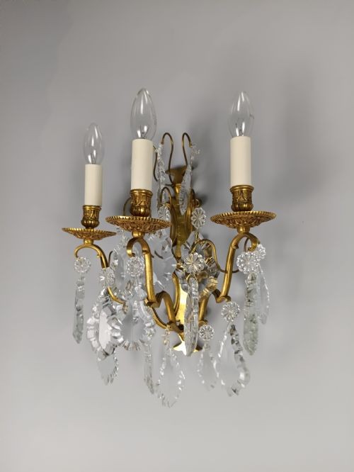 A pair of French Baroque style wall sconces featuring gilded brass frames with three arms each and hanging cut crystal drops. View IV