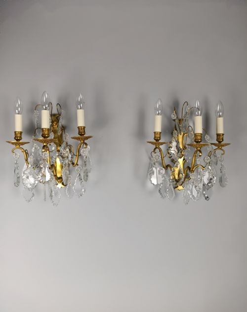 A pair of French Baroque style wall sconces featuring gilded brass frames with three arms each and hanging cut crystal drops. View V