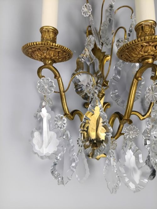 A pair of French Baroque style wall sconces featuring gilded brass frames with three arms each and hanging cut crystal drops. View VI