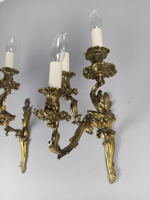 A pair of French Rococo style gilded bronze triple-arm wall sconces featuring ornate acanthus leaf metalwork and candle-style lights. View II