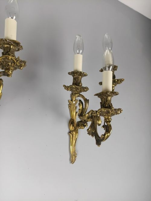 A pair of French Rococo style gilded bronze triple-arm wall sconces featuring ornate acanthus leaf metalwork and candle-style lights. View III