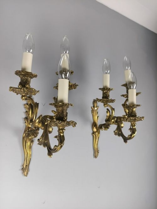 A pair of French Rococo style gilded bronze triple-arm wall sconces featuring ornate acanthus leaf metalwork and candle-style lights. View IV