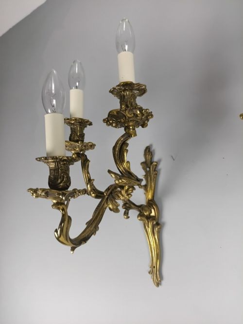 A pair of French Rococo style gilded bronze triple-arm wall sconces featuring ornate acanthus leaf metalwork and candle-style lights. View V