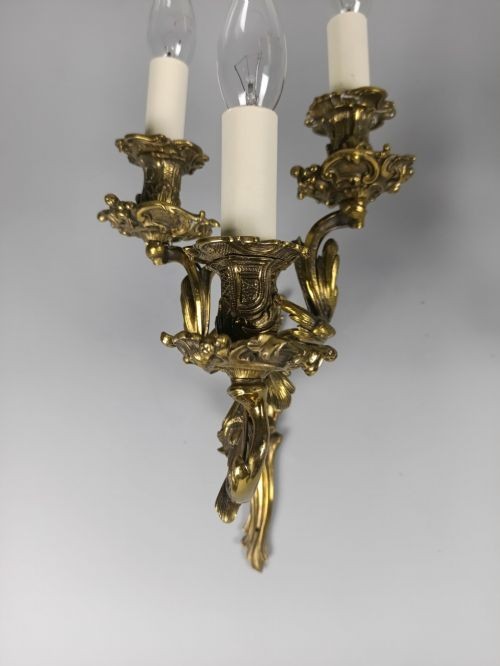 A pair of French Rococo style gilded bronze triple-arm wall sconces featuring ornate acanthus leaf metalwork and candle-style lights. View VI