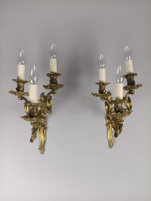 A pair of French Rococo style gilded bronze triple-arm wall sconces featuring ornate acanthus leaf metalwork and candle-style lights. View VII
