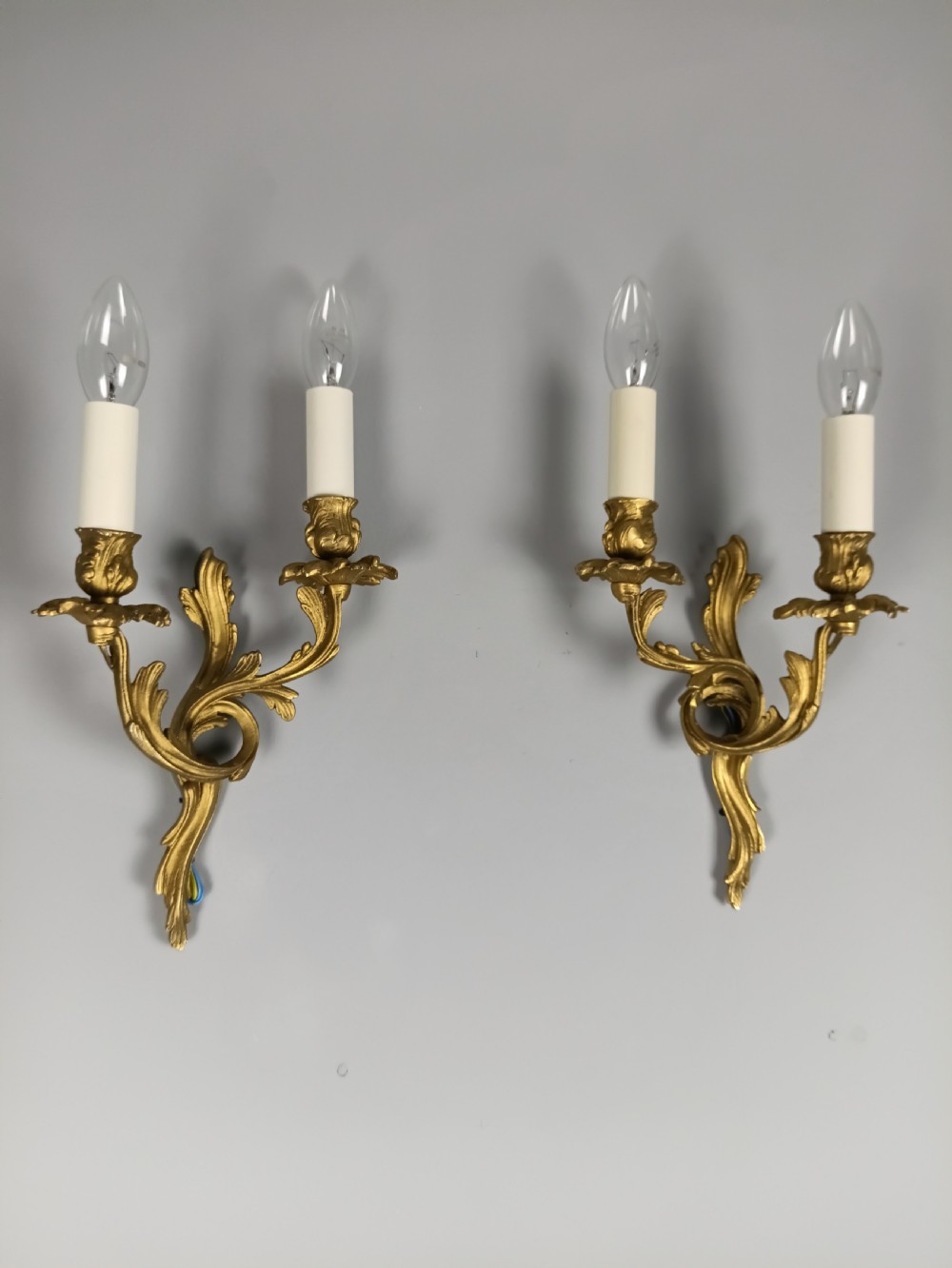 A pair of French gilt metal twin-arm wall sconces featuring scrolling acanthus leaf details and faux candle sleeves.