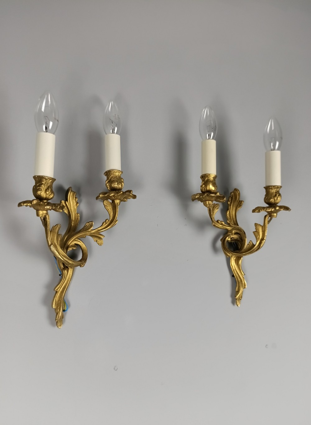 A pair of French gilt metal twin-arm wall sconces featuring scrolling acanthus leaf details and faux candle sleeves. View II