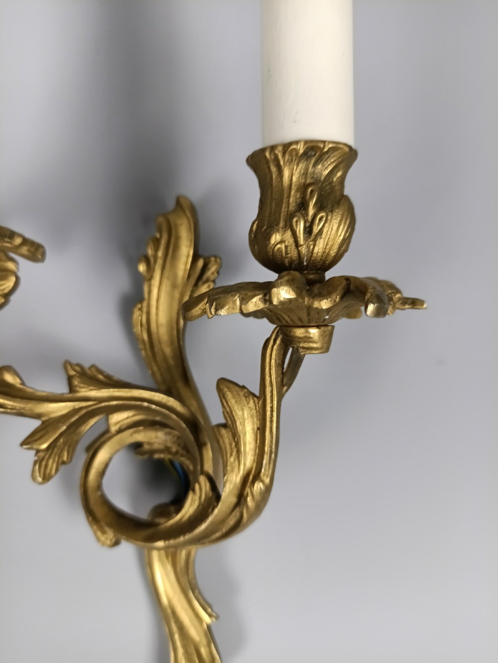 A pair of French gilt metal twin-arm wall sconces featuring scrolling acanthus leaf details and faux candle sleeves. View III