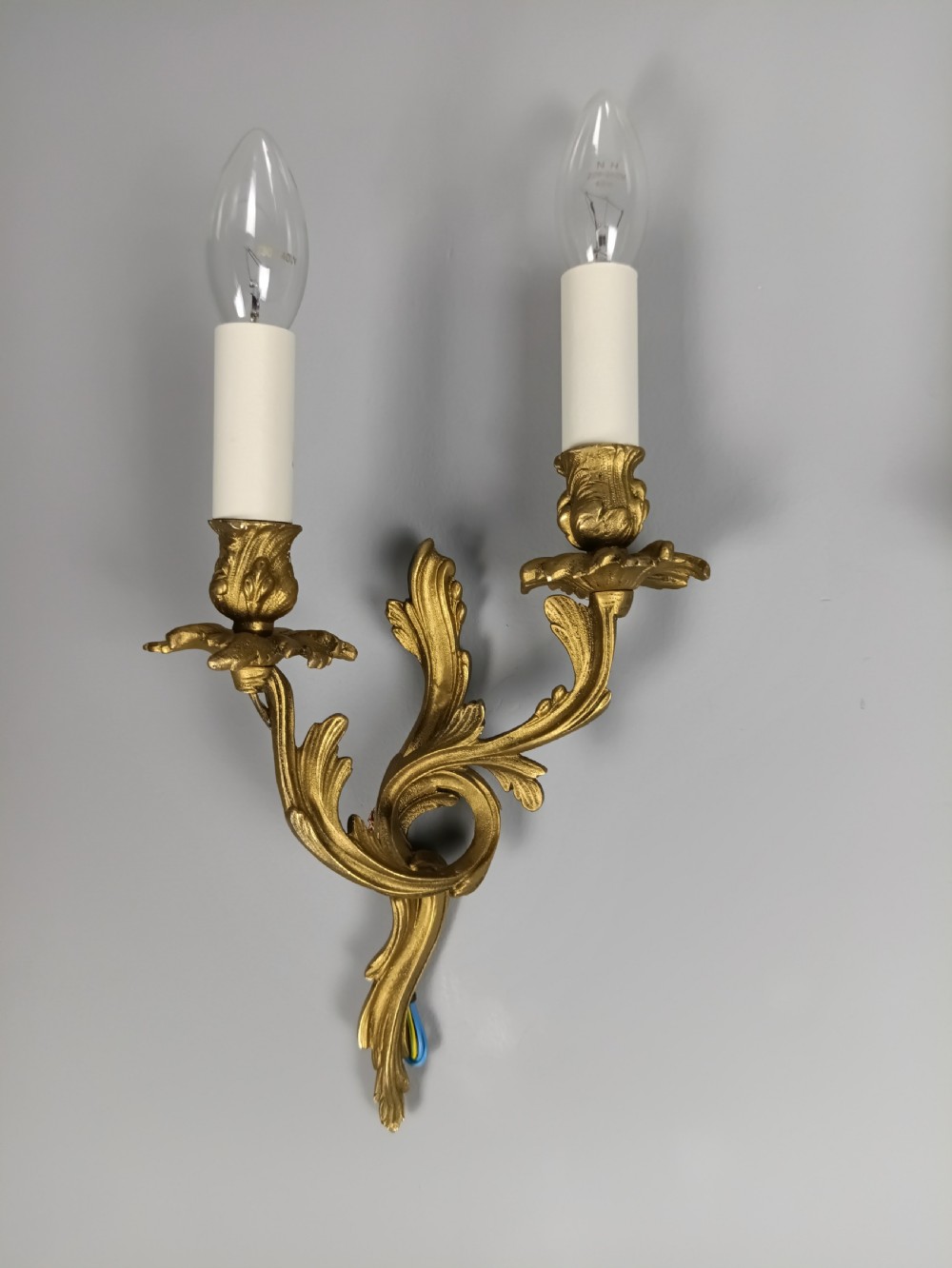 A pair of French gilt metal twin-arm wall sconces featuring scrolling acanthus leaf details and faux candle sleeves. View IV