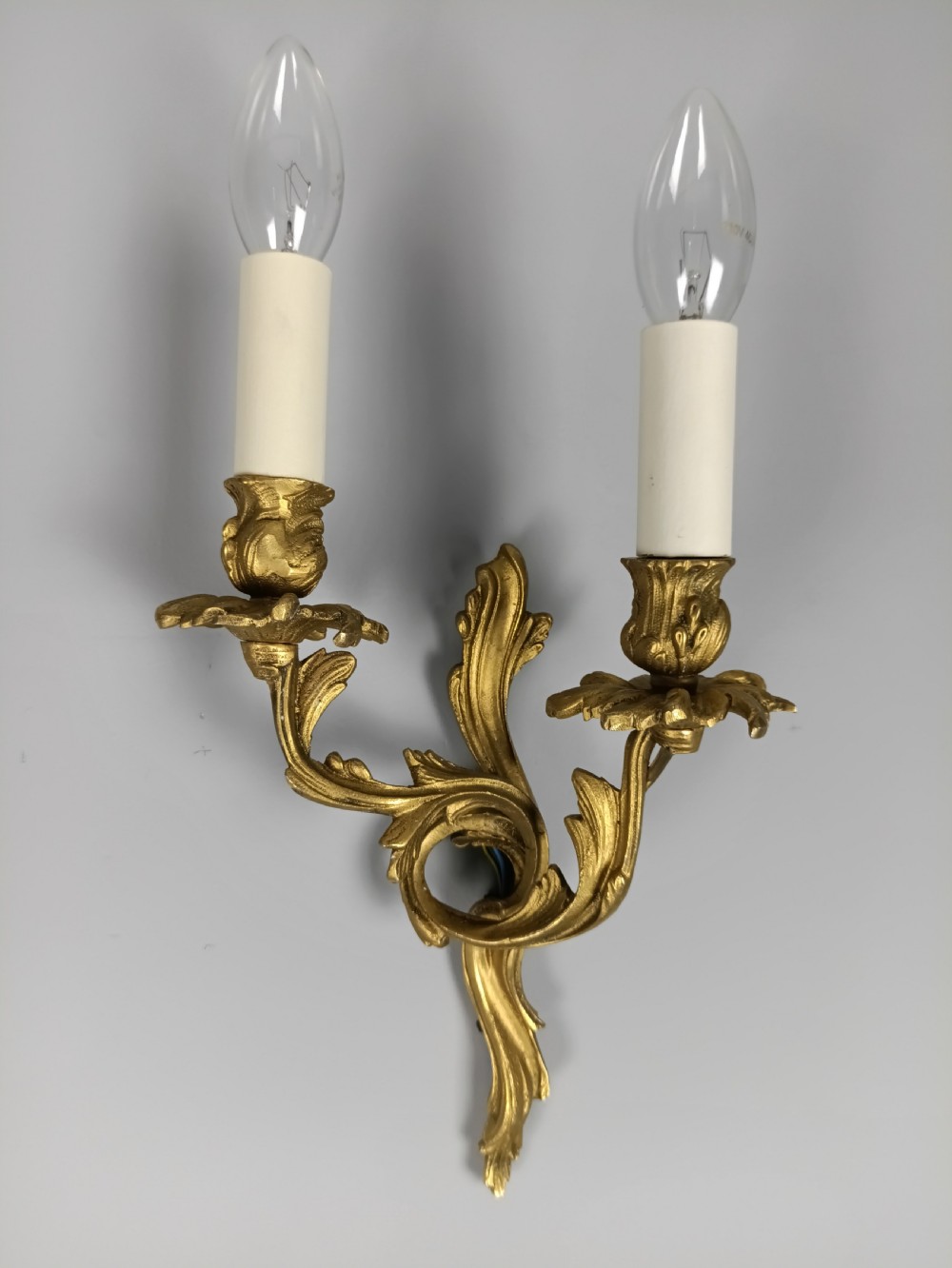 A pair of French gilt metal twin-arm wall sconces featuring scrolling acanthus leaf details and faux candle sleeves. View V