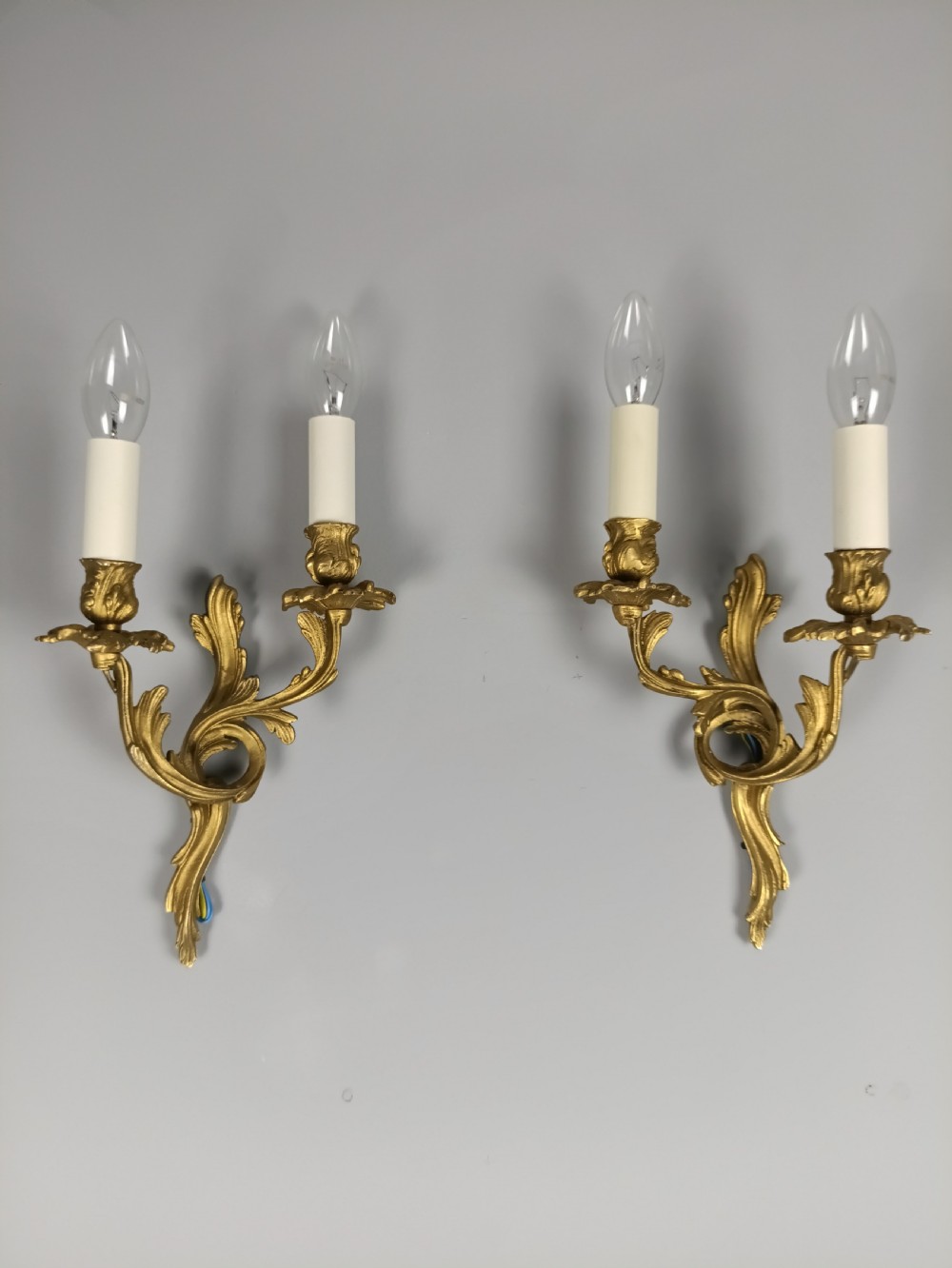 A pair of French gilt metal twin-arm wall sconces featuring scrolling acanthus leaf details and faux candle sleeves. View VI