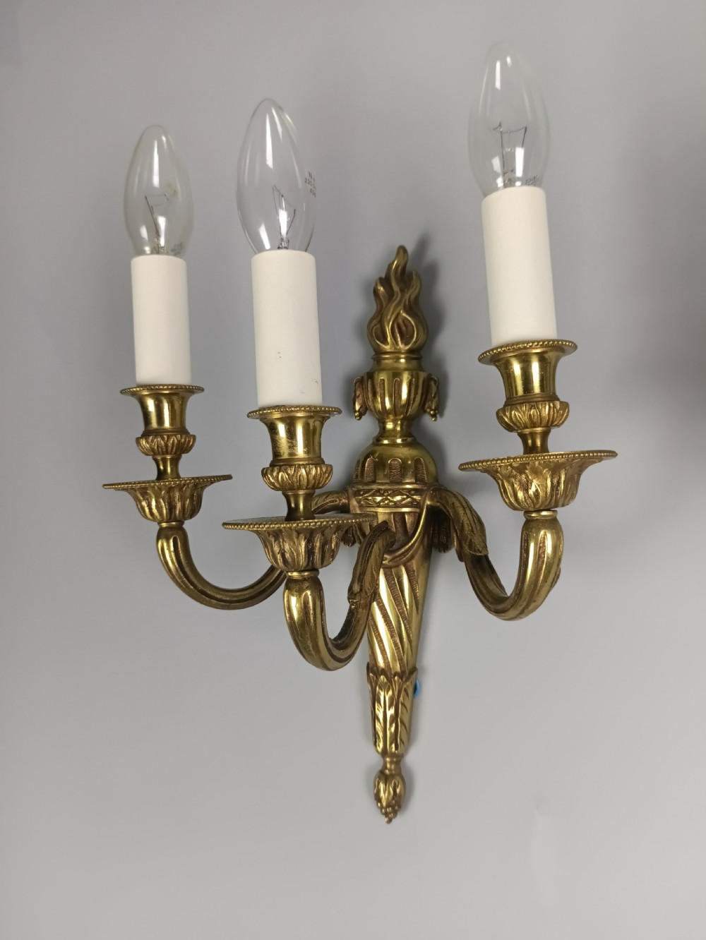 A pair of French Neoclassical gilded brass wall lights featuring three curving candle arms attached to a central tapered, fluted backplate. View II
