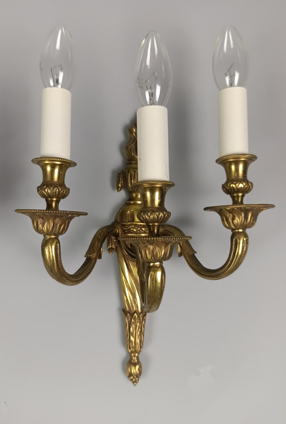A pair of French Neoclassical gilded brass wall lights featuring three curving candle arms attached to a central tapered, fluted backplate. View IV