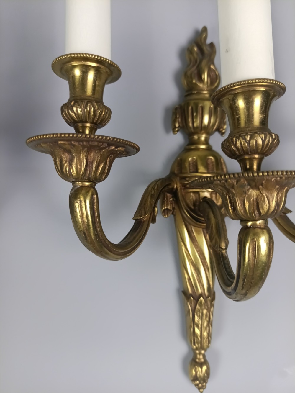 A pair of French Neoclassical gilded brass wall lights featuring three curving candle arms attached to a central tapered, fluted backplate. View V