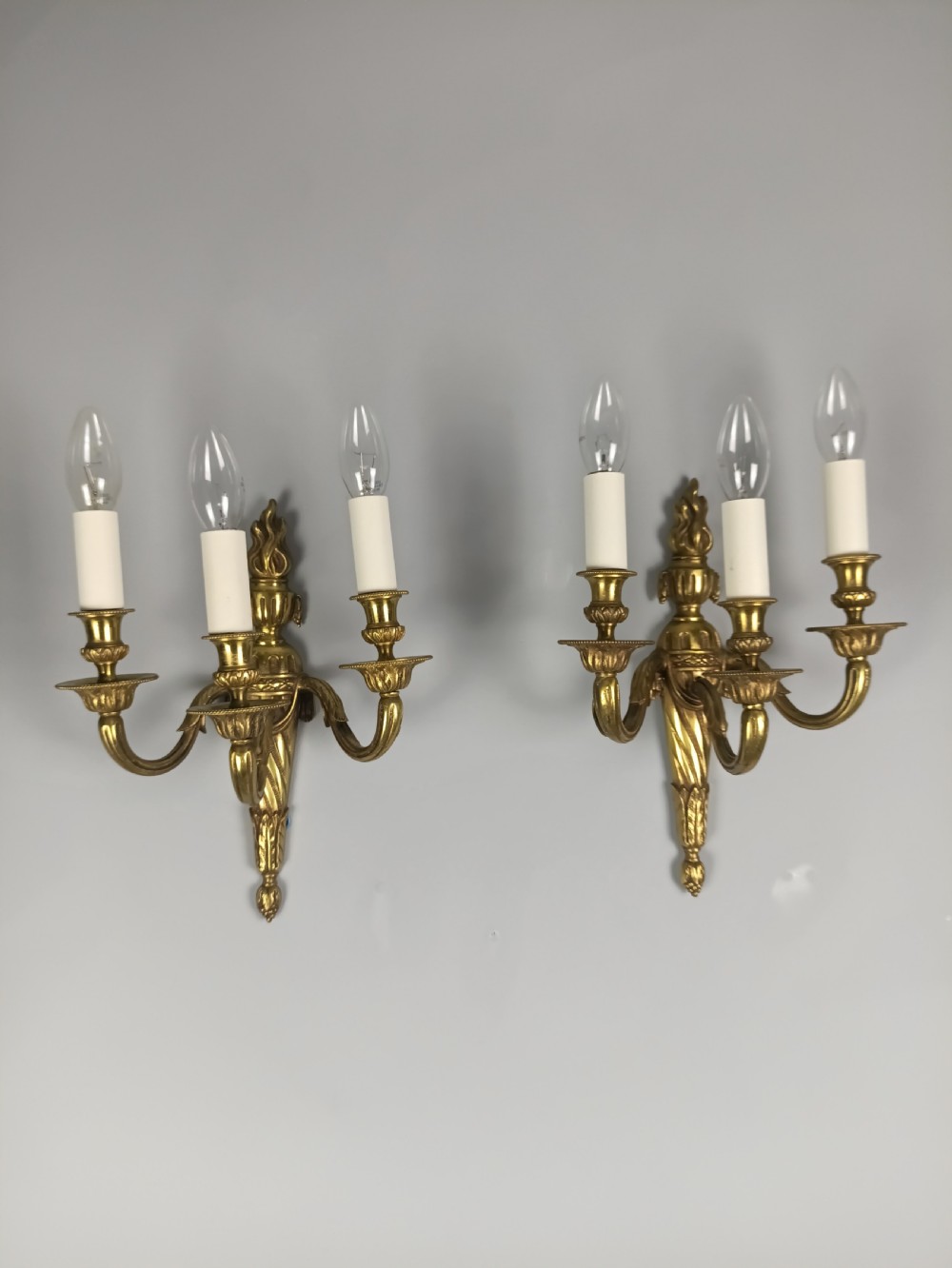 A pair of French Neoclassical gilded brass wall lights featuring three curving candle arms attached to a central tapered, fluted backplate. View VI