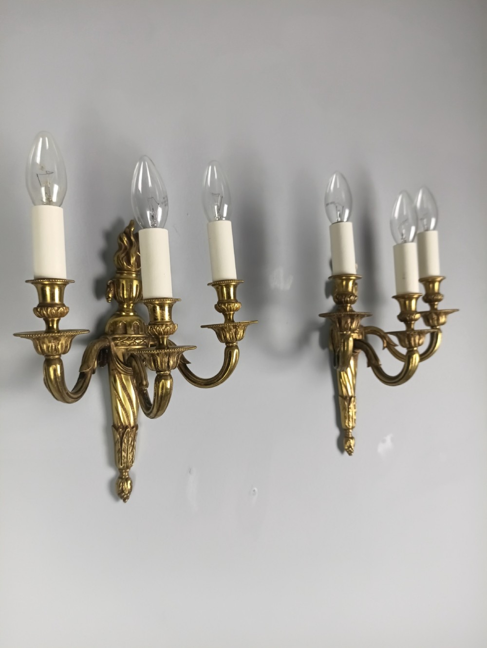 A pair of French Neoclassical gilded brass wall lights featuring three curving candle arms attached to a central tapered, fluted backplate. View VIII
