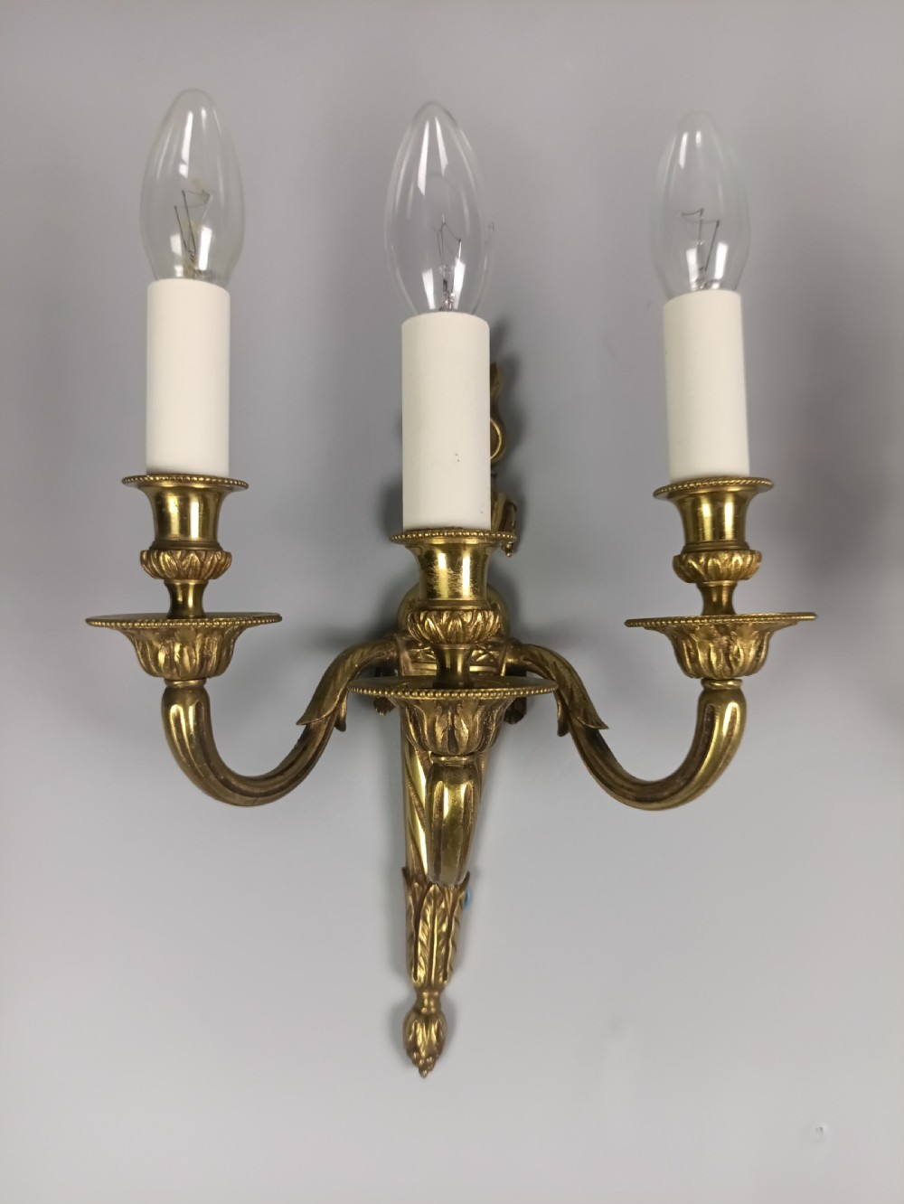A pair of French Neoclassical gilded brass wall lights featuring three curving candle arms attached to a central tapered, fluted backplate. View IX