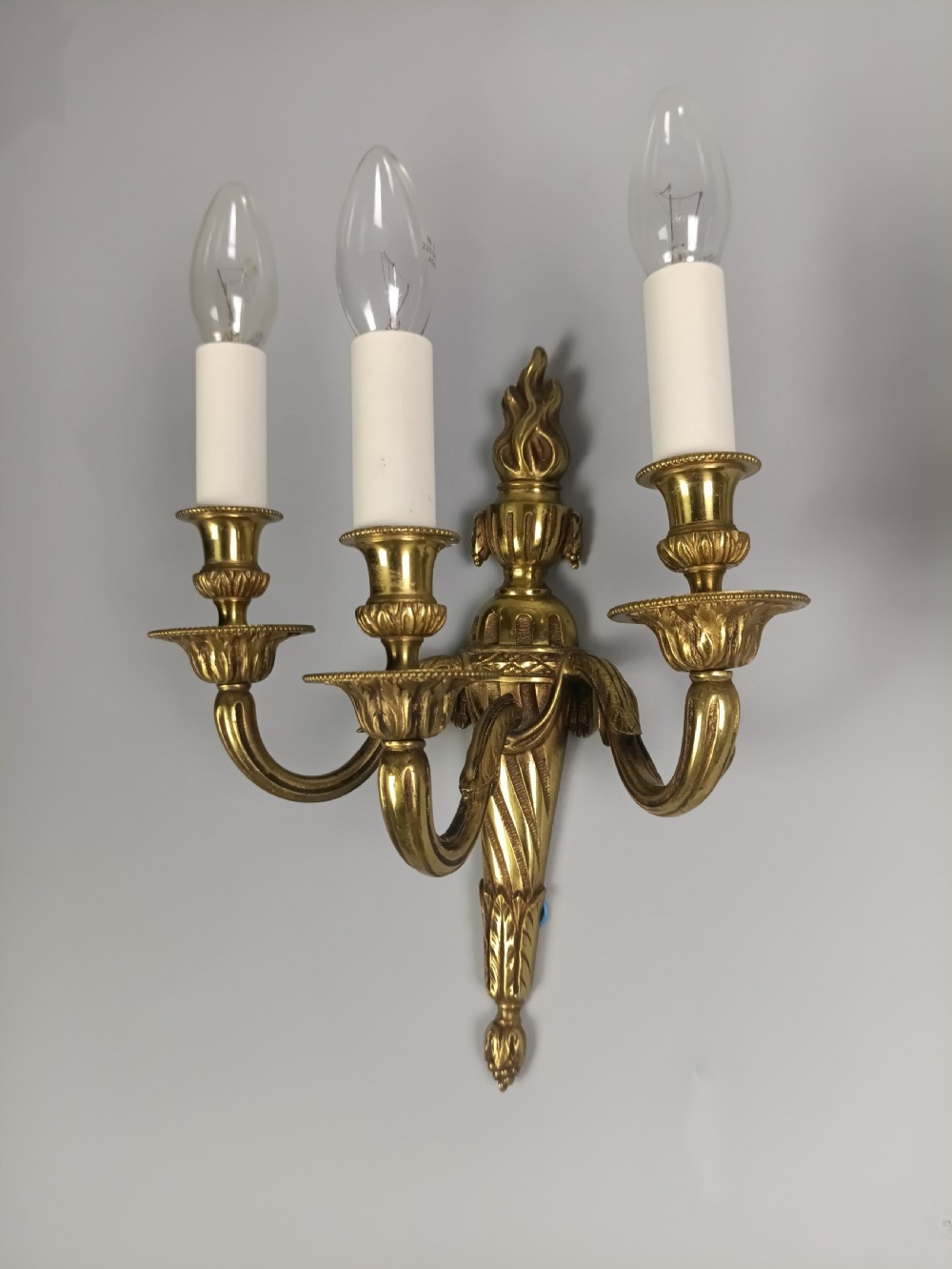 A pair of French Neoclassical gilded brass wall lights featuring three curving candle arms attached to a central tapered, fluted backplate. View X