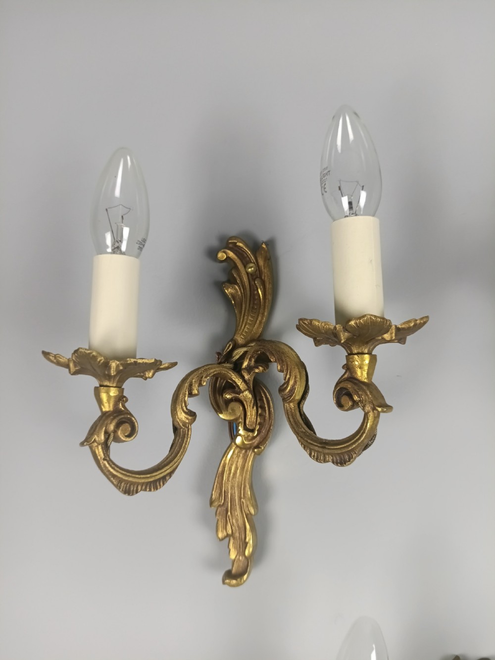 A set of three French Rococo style gilded metal twin-arm wall lights with scrollwork detailing and candle bulb fittings. View II