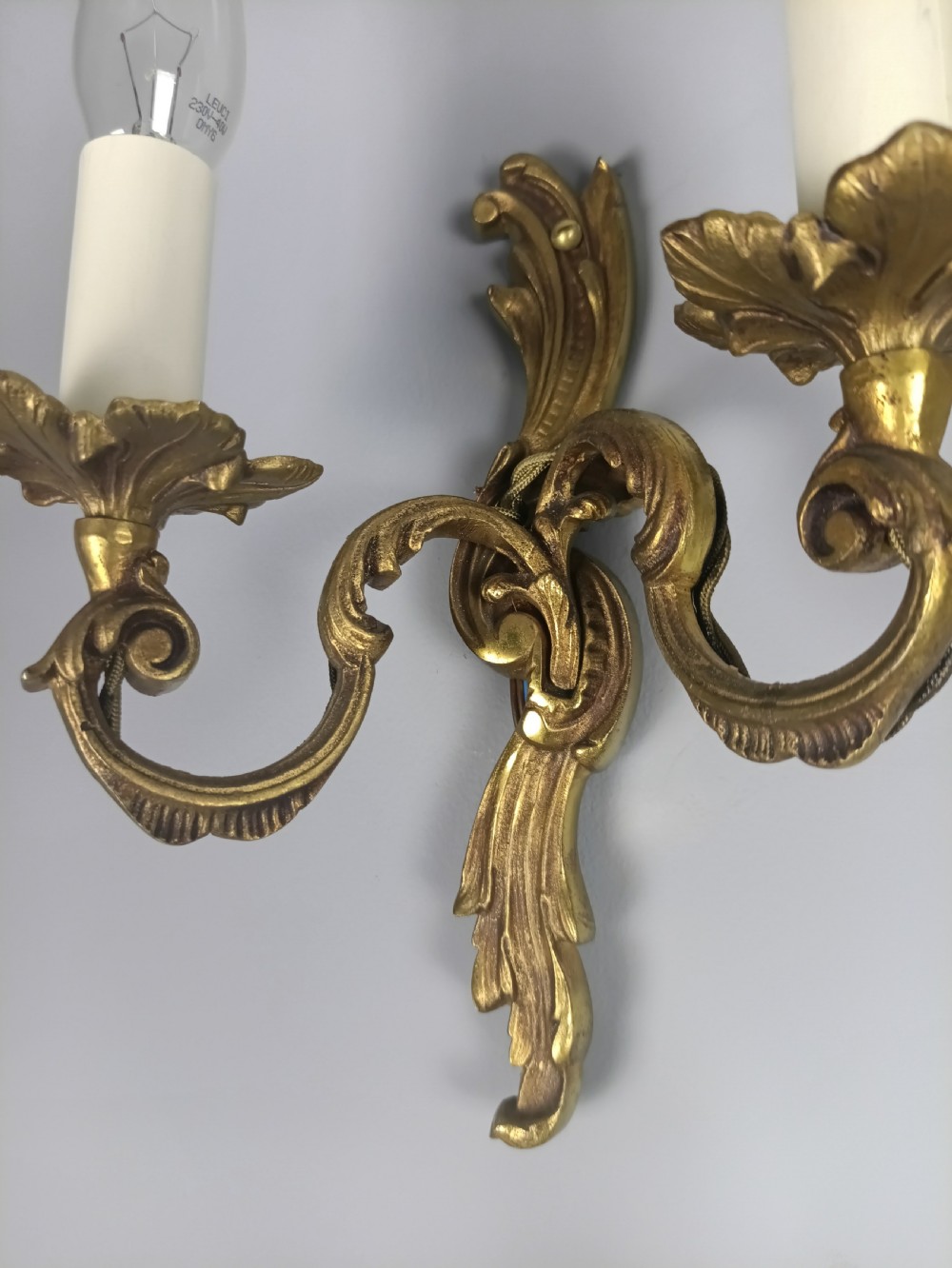 A set of three French Rococo style gilded metal twin-arm wall lights with scrollwork detailing and candle bulb fittings. View III