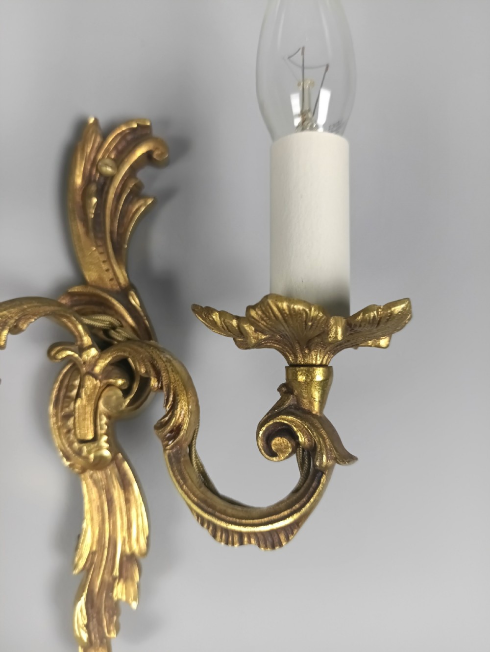 A set of three French Rococo style gilded metal twin-arm wall lights with scrollwork detailing and candle bulb fittings. View IV