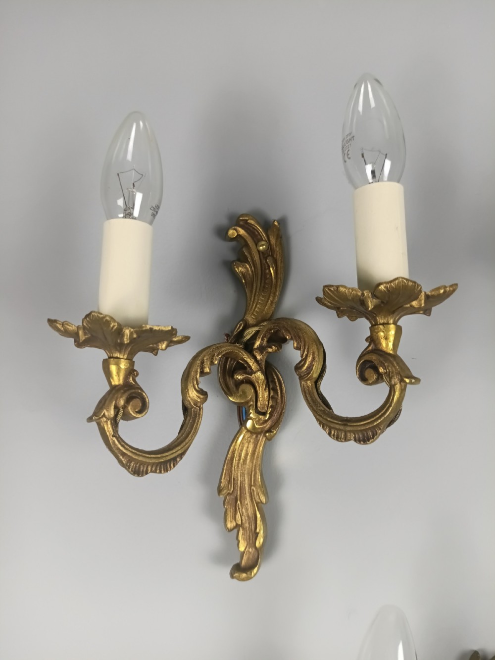 A set of three French Rococo style gilded metal twin-arm wall lights with scrollwork detailing and candle bulb fittings. View VII