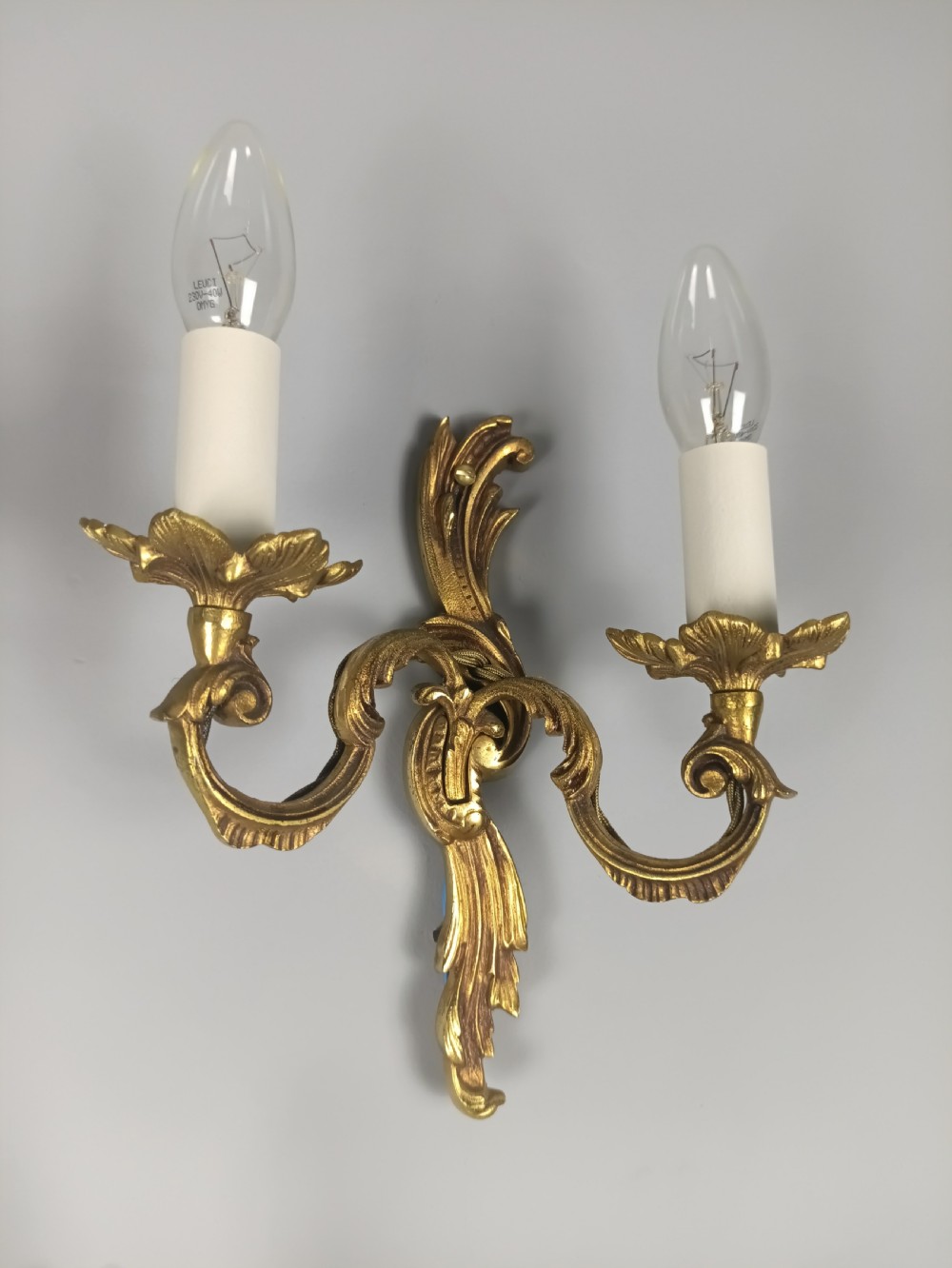 A set of three French Rococo style gilded metal twin-arm wall lights with scrollwork detailing and candle bulb fittings. View VIII